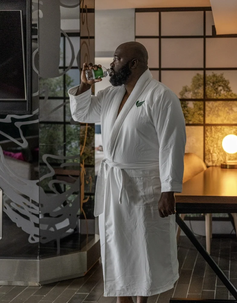 Gabriel in a white robe drinking water in a softly lit interior.