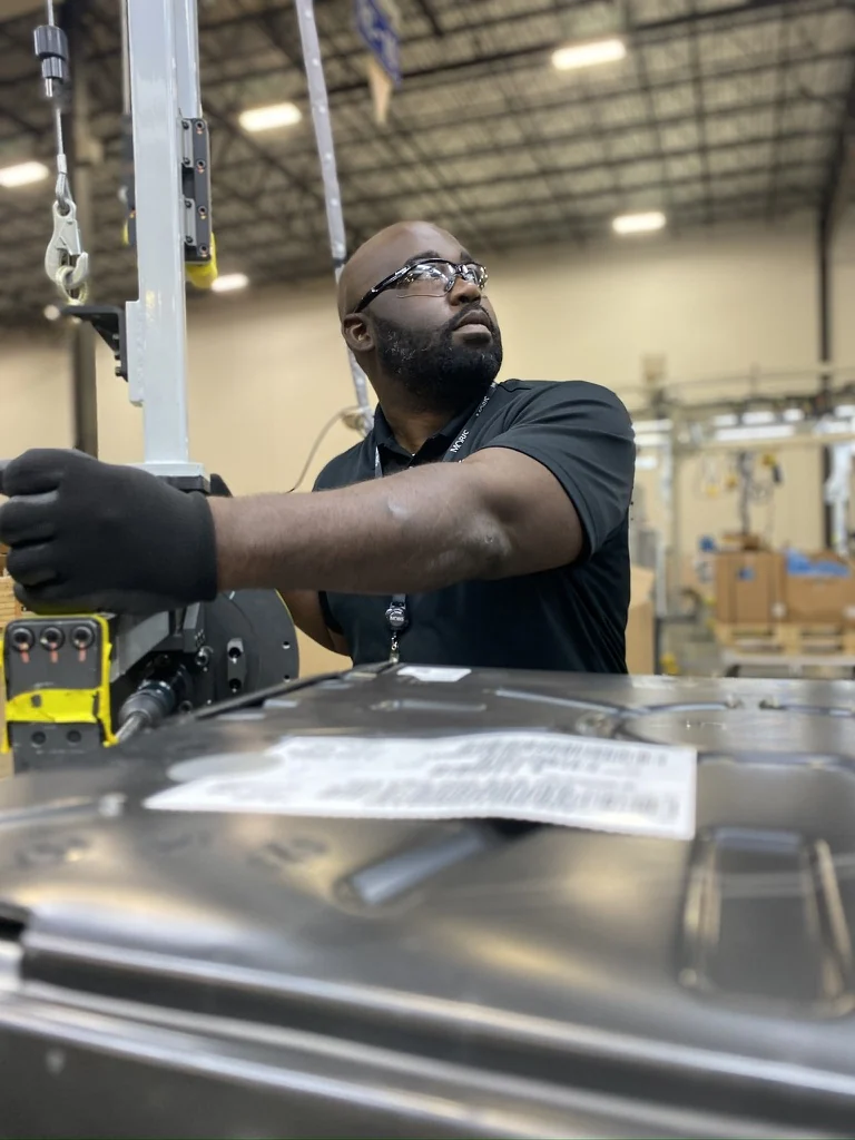 Gabriel wearing safety glasses and gloves beside equipment in an industrial workspace.
