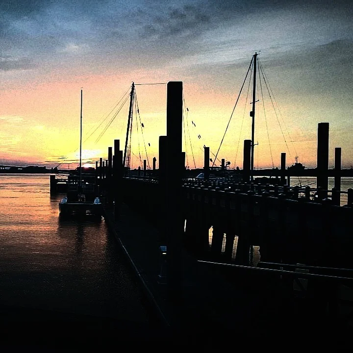 Marina and sailboat silhouettes against a sunset sky